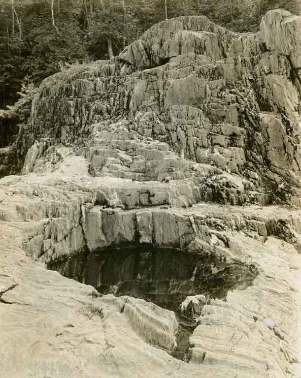 Black and white photograph of rock ledge with large, round hole
