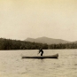 Black and white photograph of a man in a canoe with rolling hills in the background