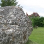 Colour photograph of a large gray rock boulder on green grass with a building in the background